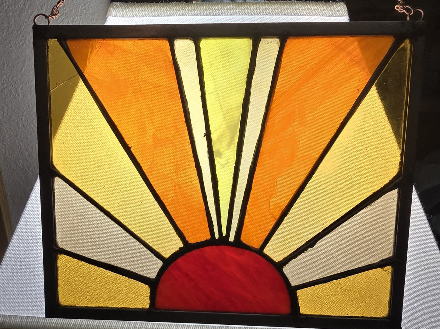 Stained glass panel with sunburst design in orange, yellow, and red on a black frame.