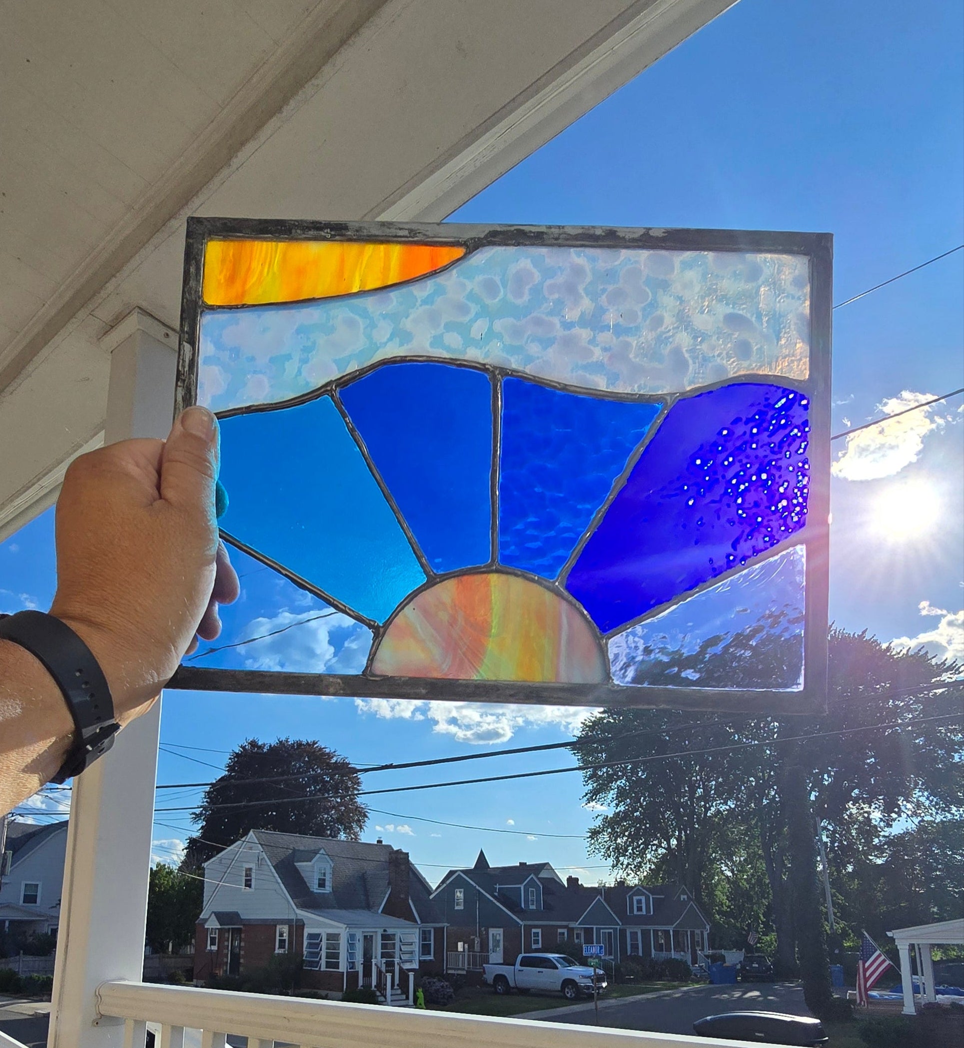 Person holding a stained glass panel against a window with a view of houses and trees.